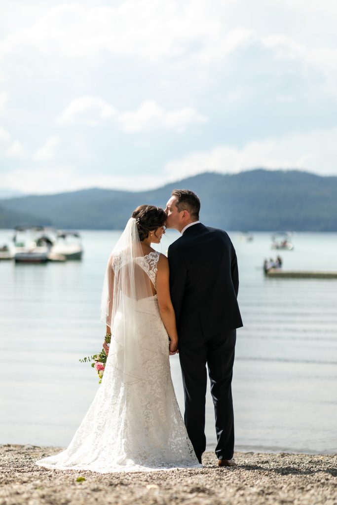 Groom kisses Bride's forehead while looking out onto Whitefish Lake in Whitefish Montana.  Be fearless in pursuit of your dreams