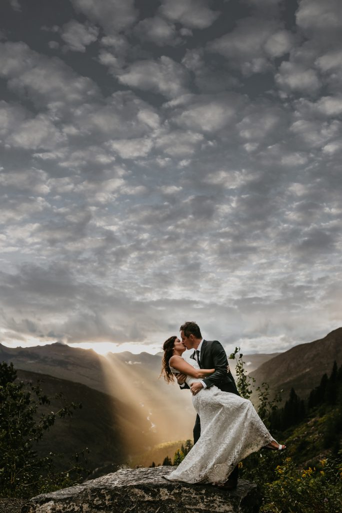 Bride and Groom in Glacier National Park with sun shining through storm clouds.  Top 3 in My Montana Wedding 2020 cover contest.  Be fearless in pursuit of your dreams